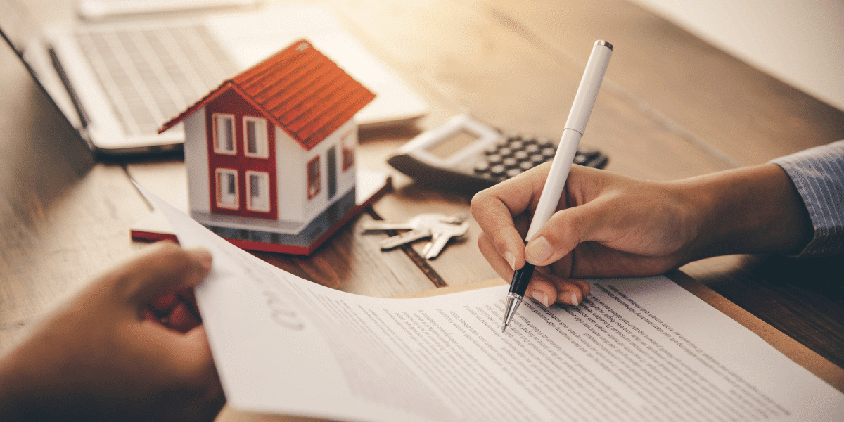 A person signing a lending document with a model house demonstrating that it is a mortgage contract