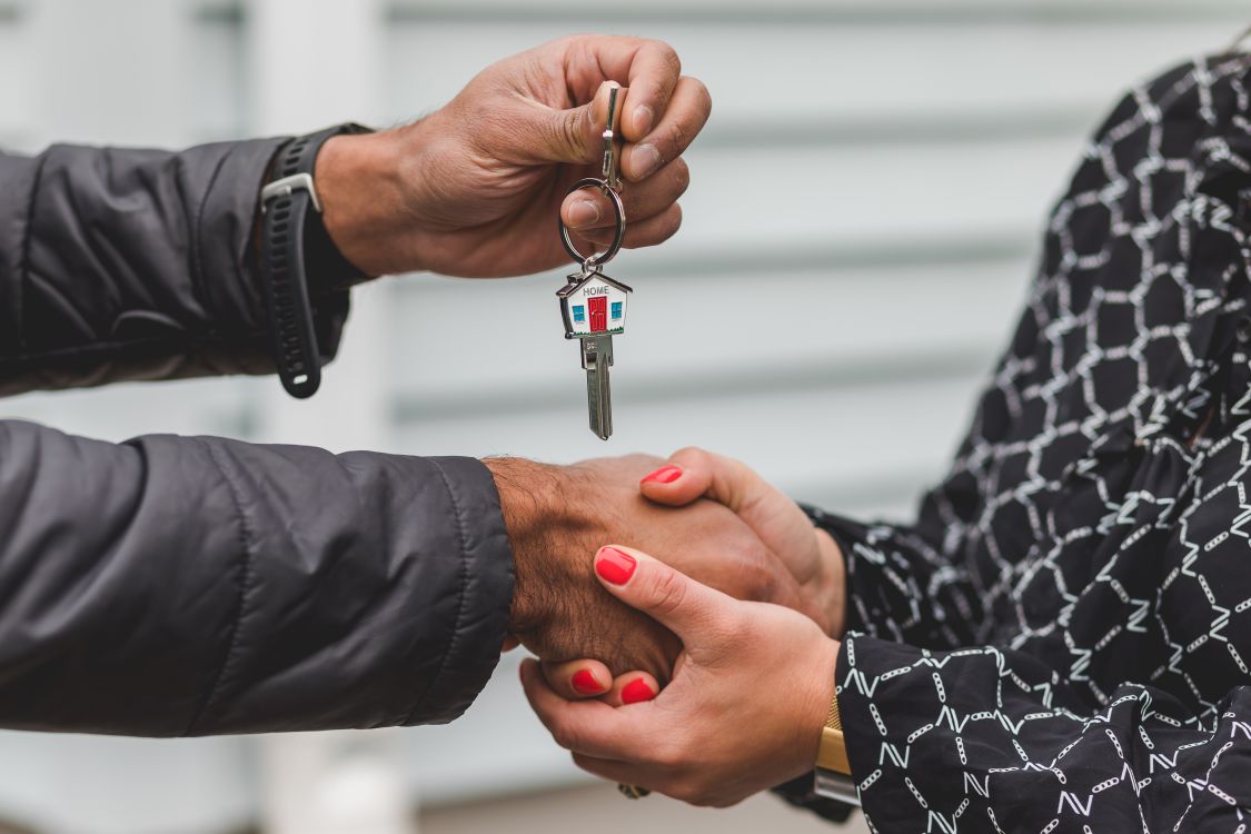 A person's hand carefully places a coin into a white, house-shaped piggy bank, symbolizing the act of saving money and retaining equity when selling a home.