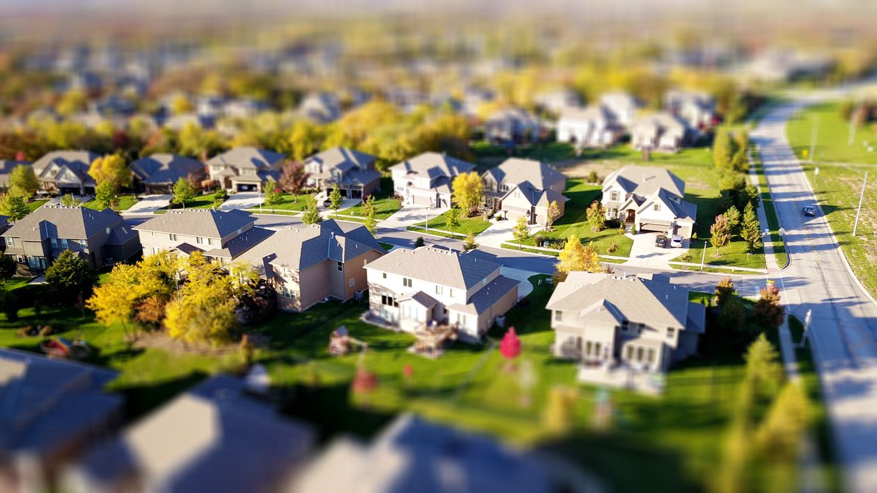 A person's hand carefully places a folded bill into a white ceramic piggy bank shaped like a house, symbolizing savings and home equity.