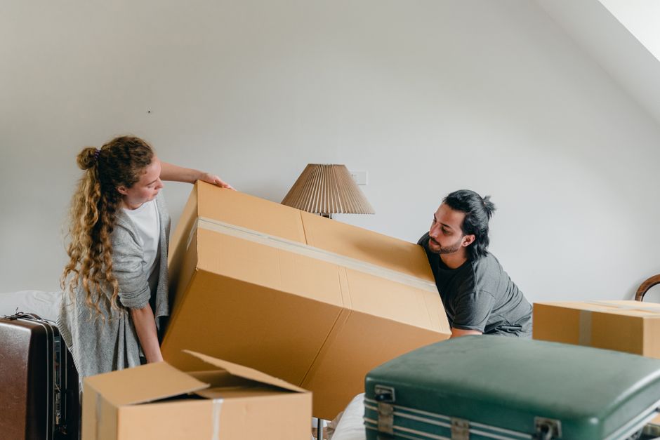 Professional, happy couple carries moving boxes into their new, modern suburban home on a bright, sunny day, representing ...