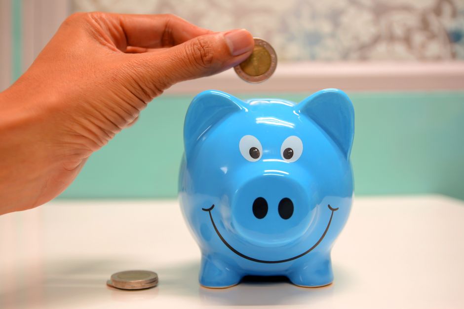 A close-up of a person's hands placing money into a house-shaped piggy bank, symbolizing saving on real estate commissions and keeping more profit.