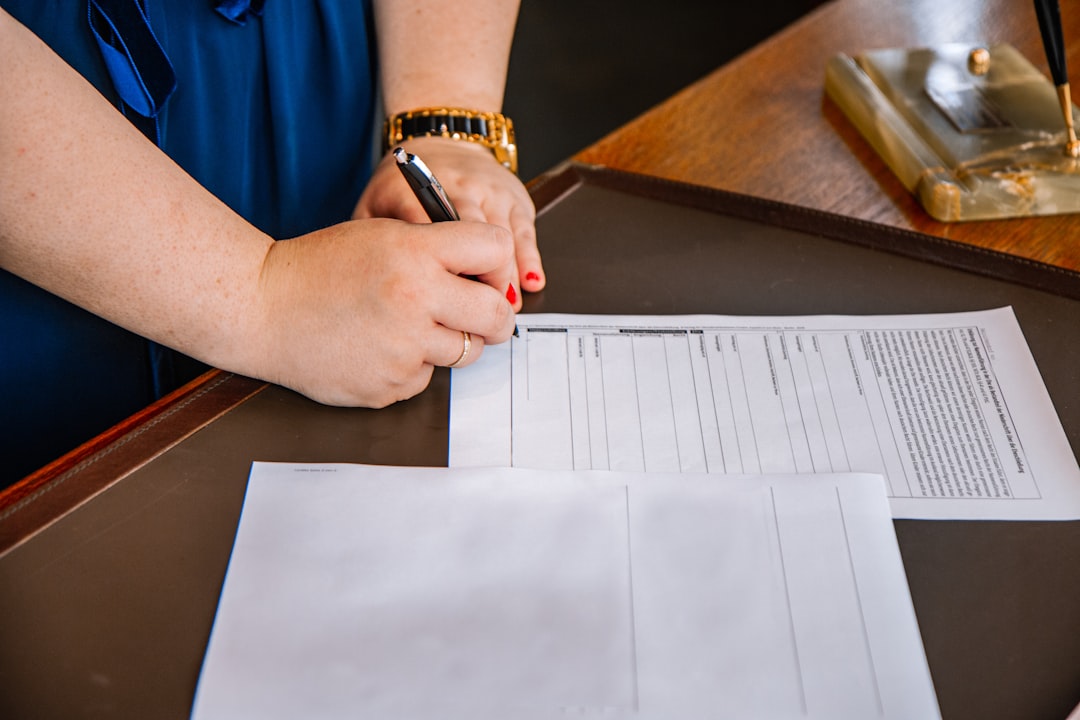 Close-up, professional shot of a person's hands signing a formal real estate document with a pen on a clean wooden table, ...