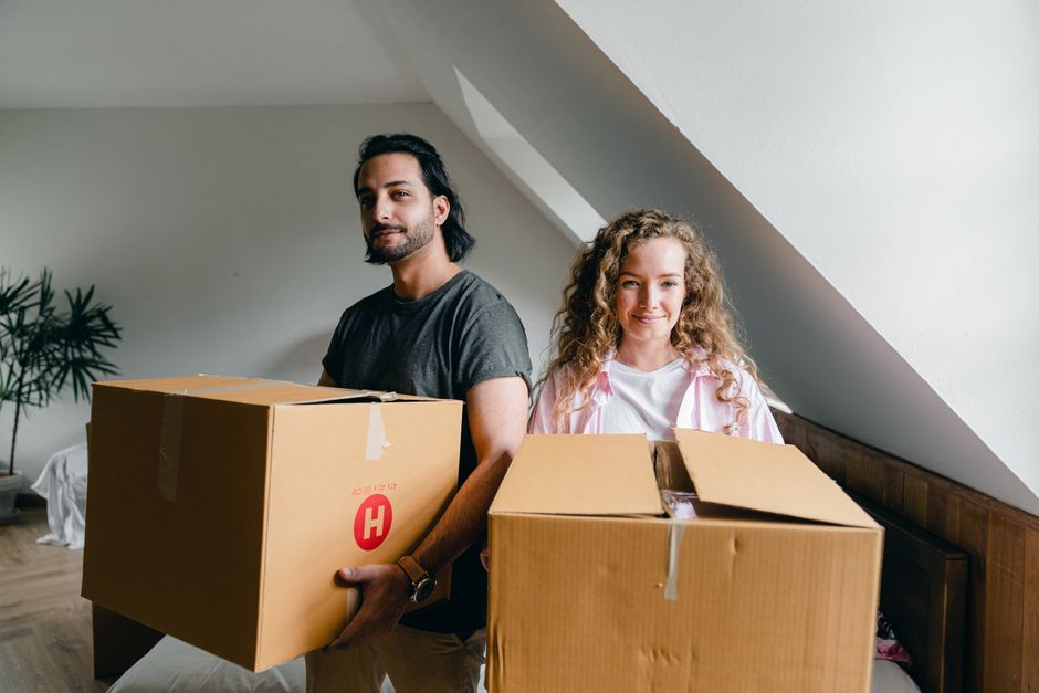 A joyful young family with children smiling while carrying moving boxes into their beautiful new modern home, illustrating the success of a 'move-up' home purchase.
