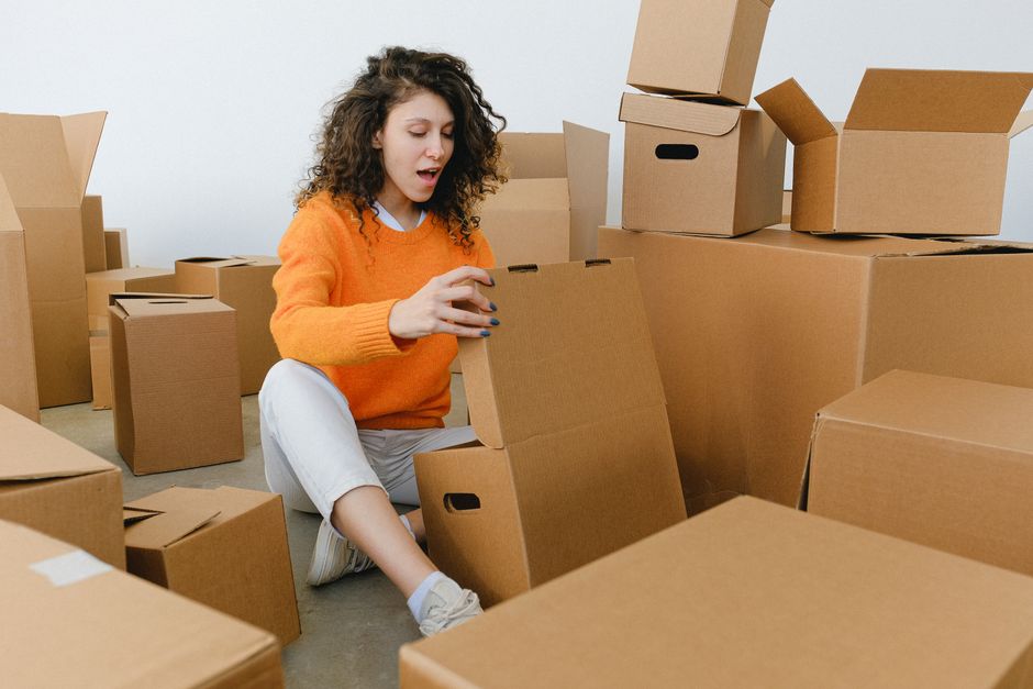 A tired but resolute homeowner sits on the floor surrounded by packing boxes, illustrating the emotional and physical effort required to sell a home and keep your sanity.